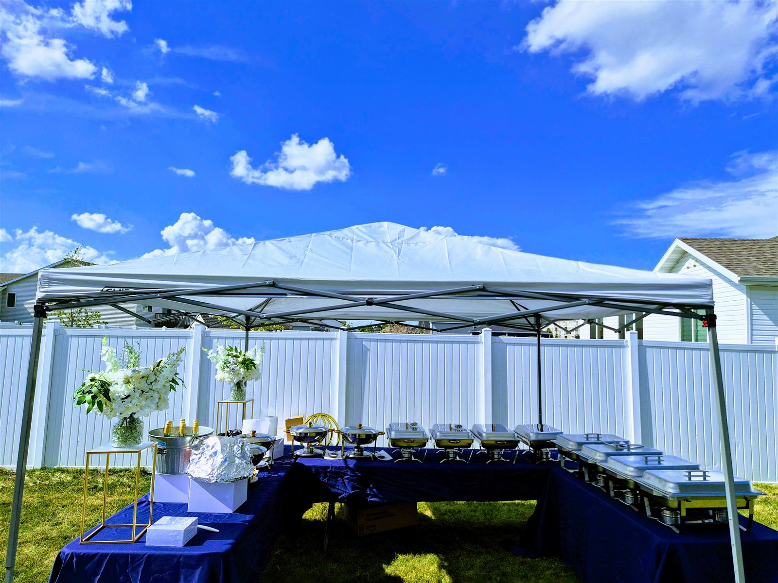 Outdoor catering buffet setup with chafing dishes, navy linens, and a chilled drink station under a canopy tent